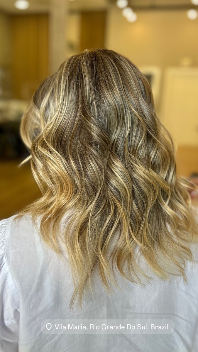 Cabelo iluminado em tons dourados com finalização em ondas